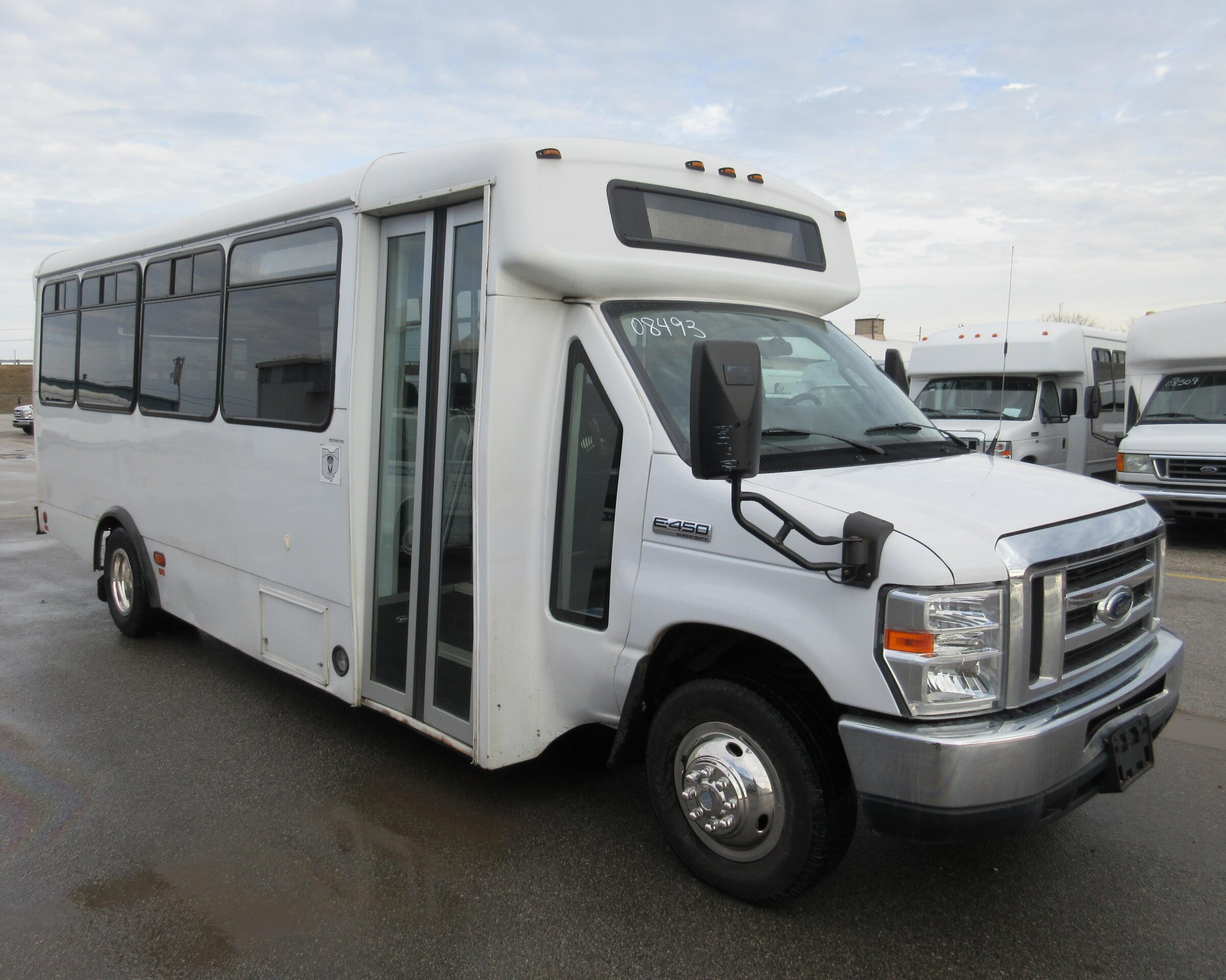 A white mid-sized shuttle bus parked on a paved lot, with large side windows, a front passenger door, and a Ford E-450 front cab.