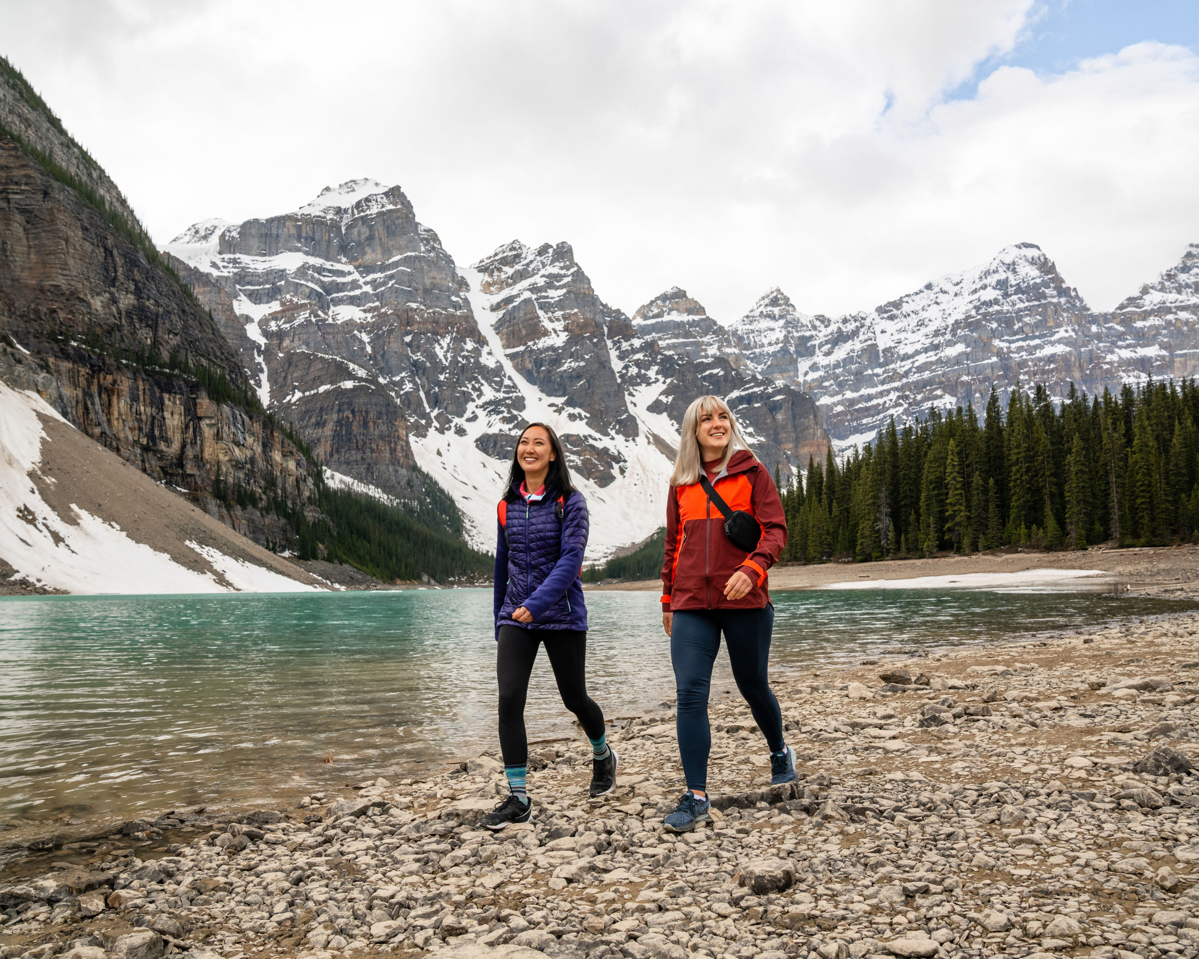 Two people walk on the rocky beach beside Moraine Lake in Banff National Park
