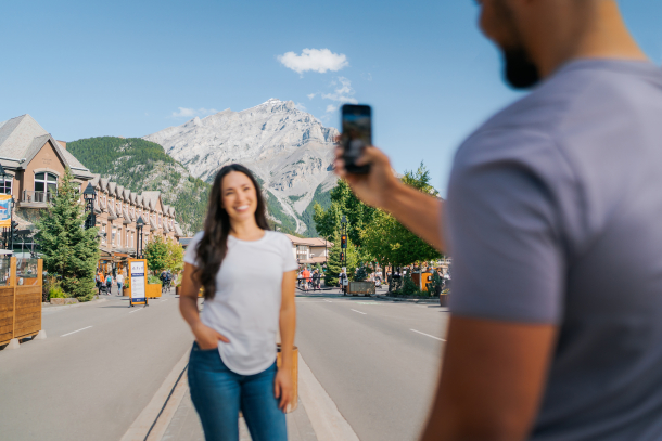 A couple takes a photo on the Banff Avenue Pedestrian Zone with Cascade Mountain in the background