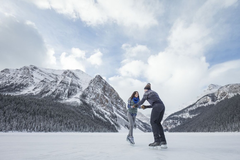 Couple holding hands while ice skating, mountains in the background, at Lake Louise in Banff National Park
