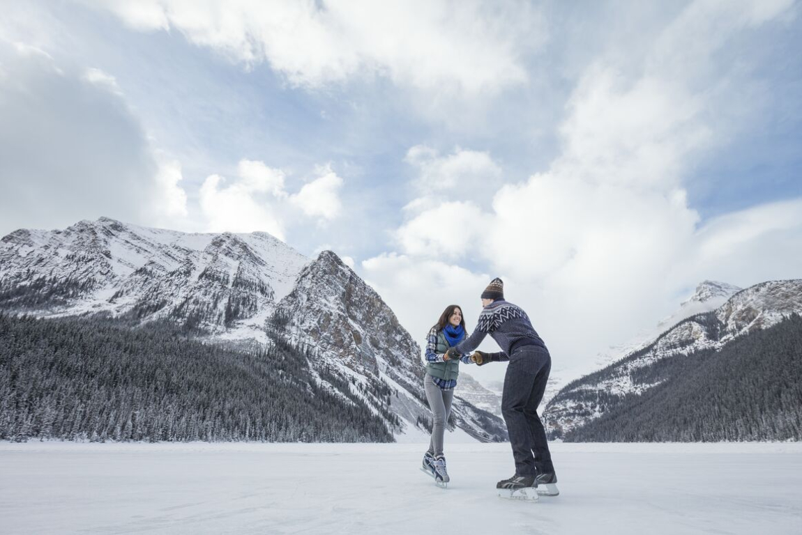 Couple holding hands while ice skating, mountains in the background, at Lake Louise in Banff National Park