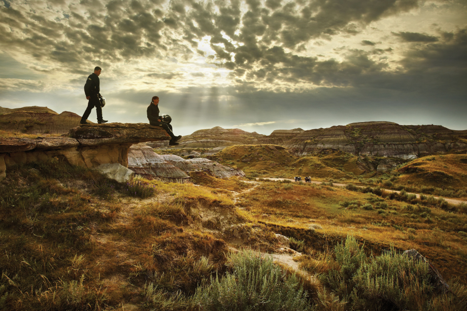Two men in motorcycle gear sitting on the edge of a cliff at sunset overlooking dinosuar provincial park