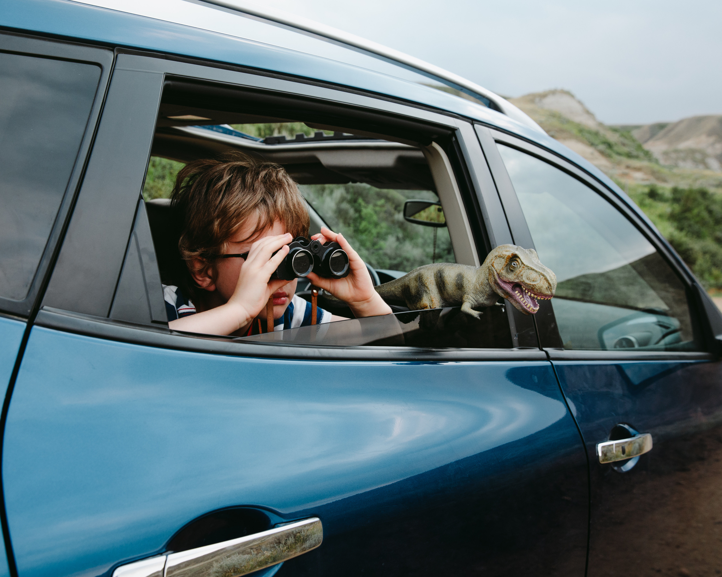 Boy / child in a car with a dinosaur toy and looking through binoculars