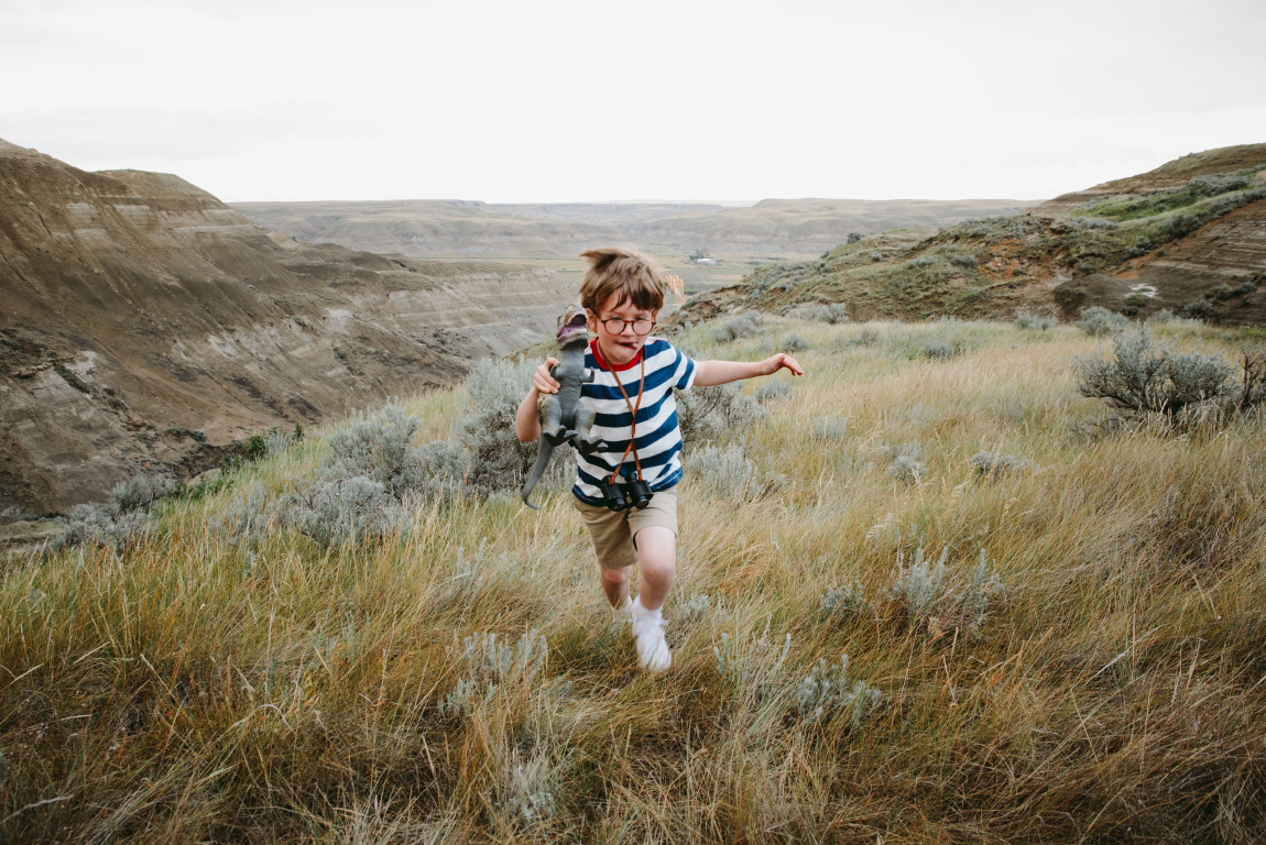 Boy / child running / hiking through a meadow in the Canadian Badlands with a dinosaur toy