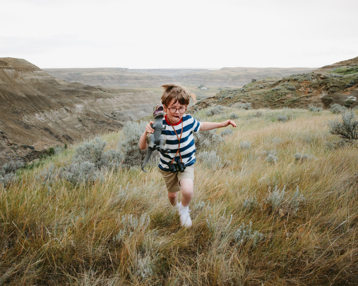 Boy / child running / hiking through a meadow in the Canadian Badlands with a dinosaur toy