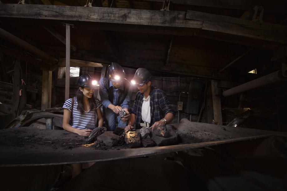 Couple / man and woman wearing mining hats and looking at coal with a guide inside Atlas Coal Mine