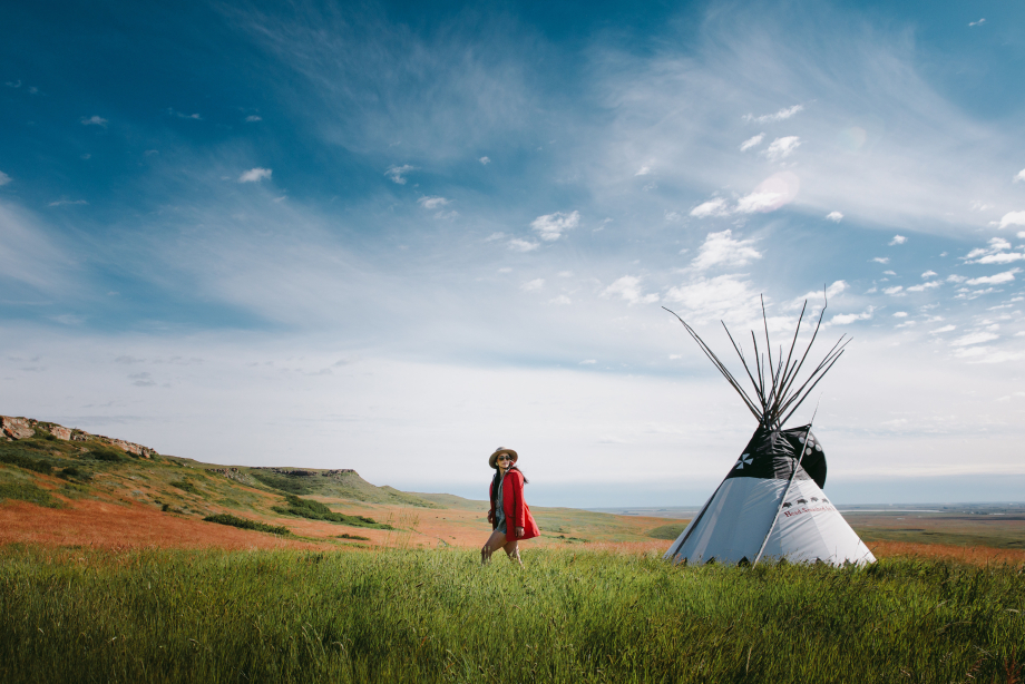 Woman walking past a tipi in a meadow at Head-Smashed-In Buffalo Jump in Southern Alberta
