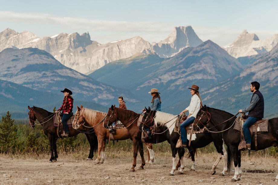 A group of horseback riders line up on their horses with mountain views in the background while horseback riding at Boundary Ranch in Kananaskis Country