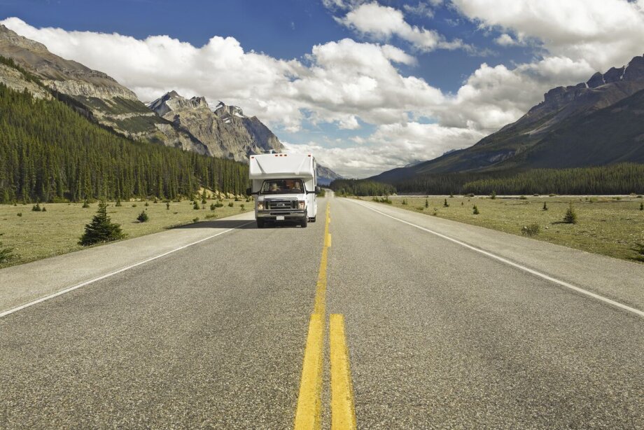RV driving down the road with the mountains in the background
