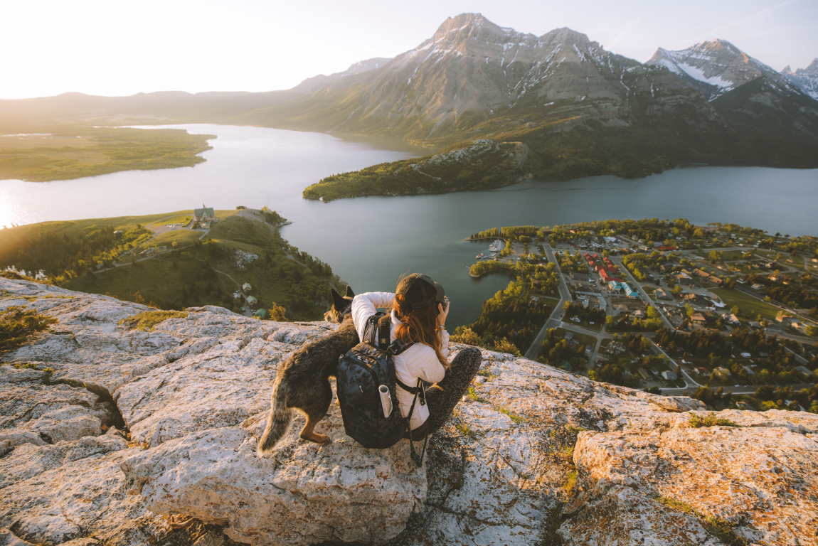 Scenic shot of woman and a dog sitting on rocks /hiking and taking a picture of the water and mountains in the distance