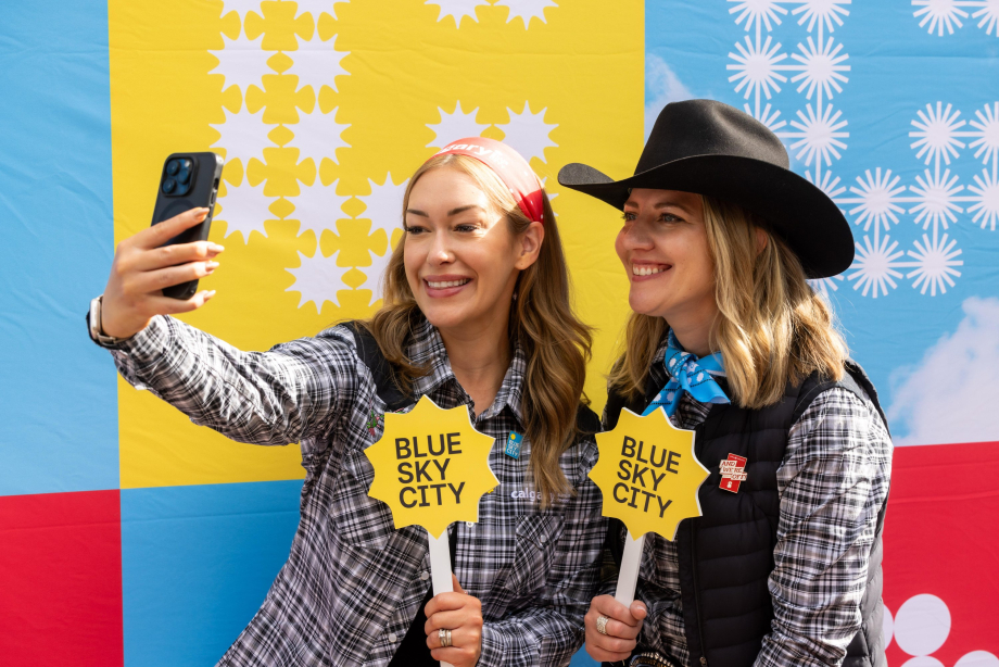 Two women dressed in western attire posing for a selfie with blue sky city paraphernalia