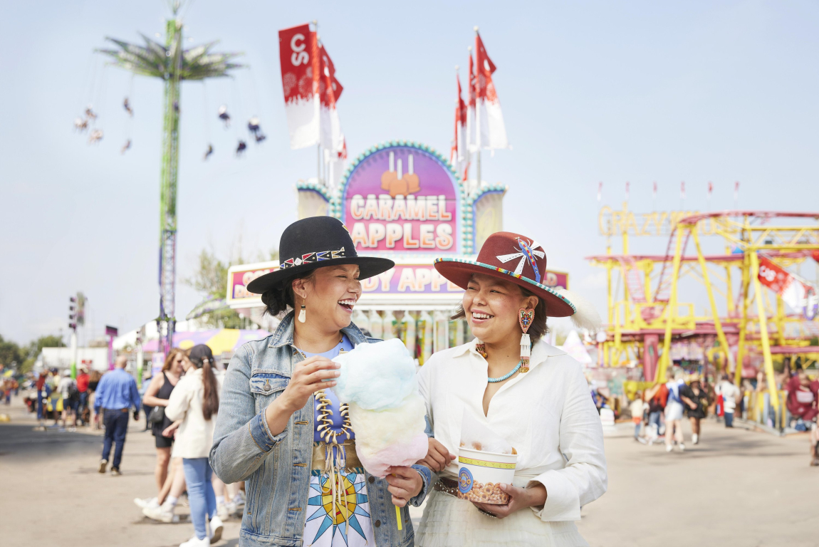 Two indigenous women laughing and eating cotton candy at the midway of the Calgary Stampede