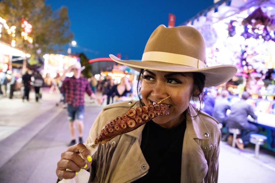 A girl trying unique fair foods, an octopus tentacle on a stick.