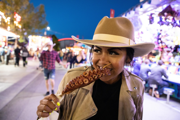 A girl trying unique fair foods, an octopus tentacle on a stick.