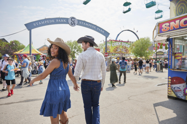 Couple dressed in western wear walking hand in hand down the Calgary Stampede midway