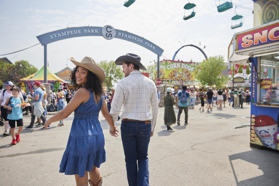 Couple dressed in western wear walking hand in hand down the Calgary Stampede midway