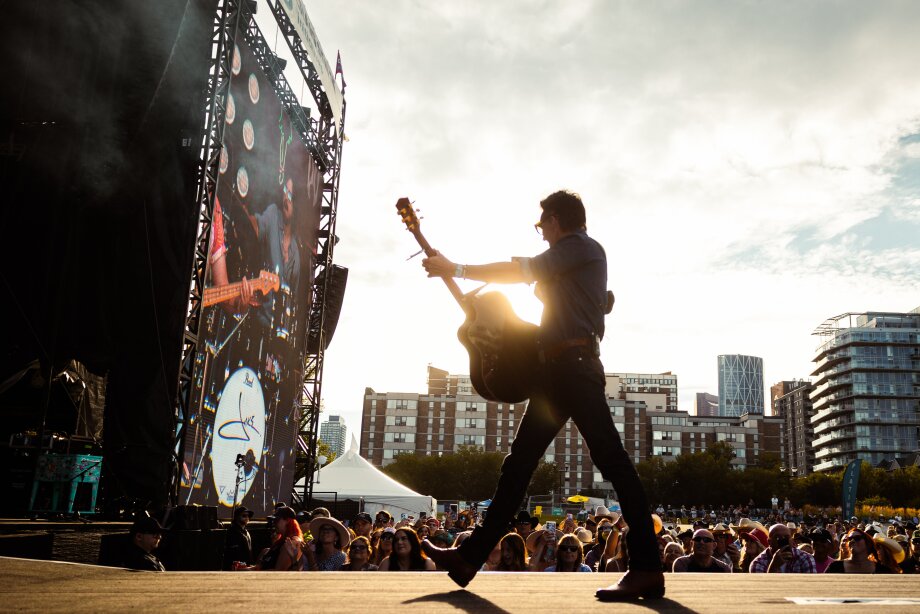 A performer with a guitar on the stage at Country Thunder with downtown in the background.