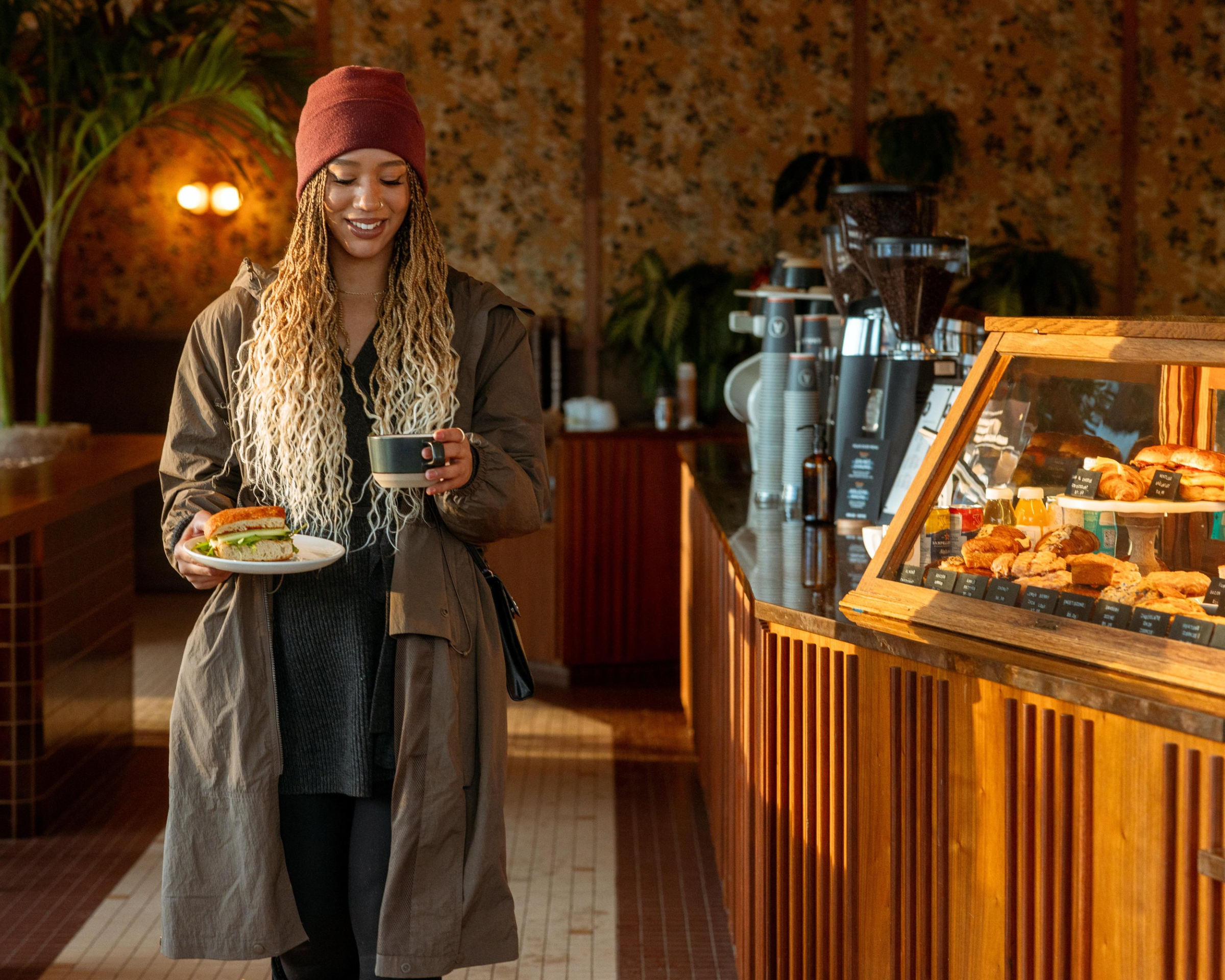 Woman walking with a sandwich and coffee through a cafe.