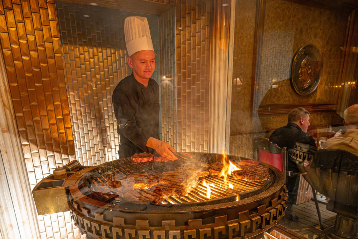 A chef cooking steaks on a large grill at Caesar's Steakhouse.