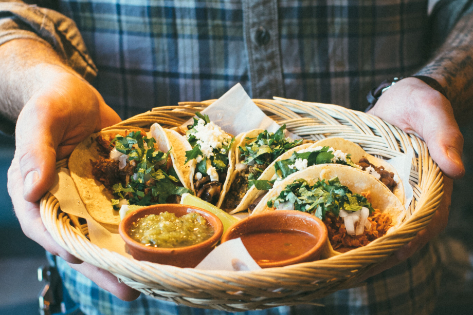 Man holding a plate of tacos at Native Tongues Taqueria in Calgary
