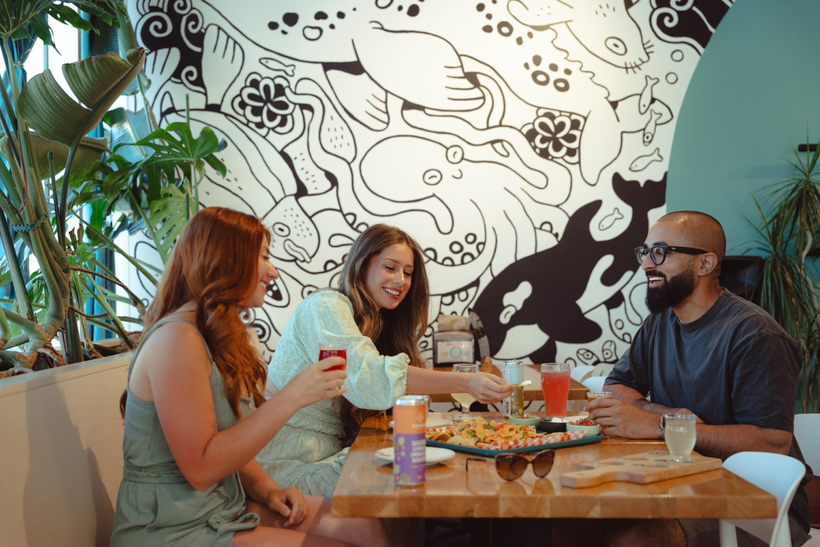 Three friends eating at Rising Tides restaurant in Bowness, on a sunny summer evening.