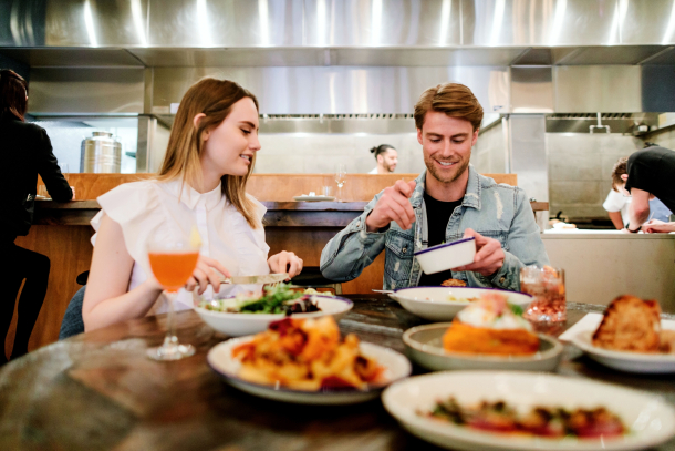 Couple drinking and eating at a restaurant / bar with open kitchen behind them in Calgary