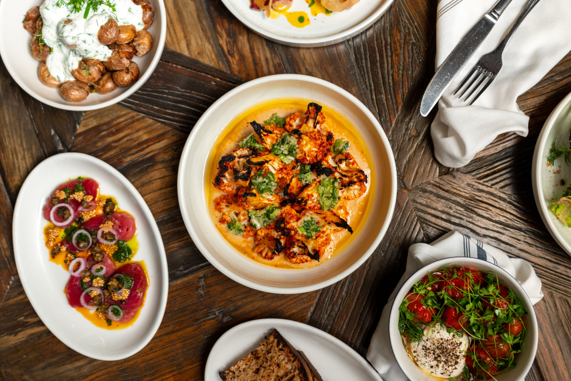 A top down image of a main dish with sides laid out throughout the table with cutlery laid out beside it