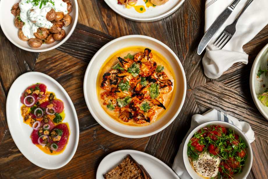 A top down image of a main dish with sides laid out throughout the table with cutlery laid out beside it