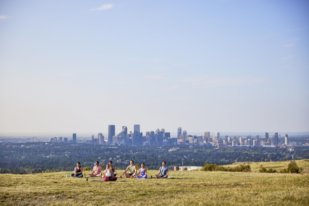 group practices yoga in Nose Hill Park with the Calgary skyline in the background