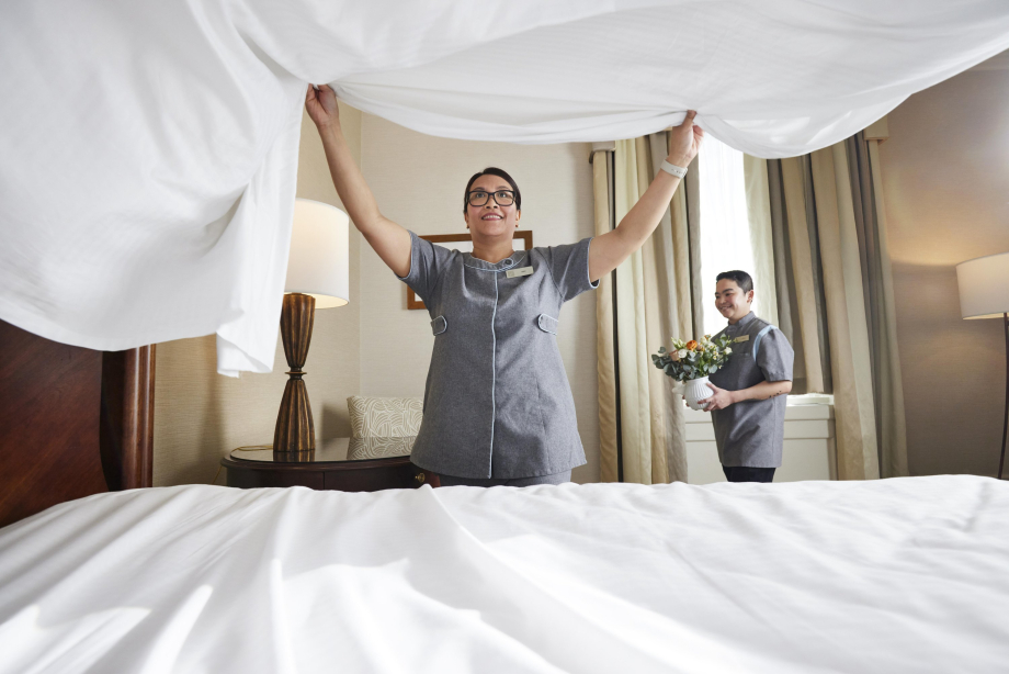 Housekeepers maiking a bed and bringing in flowers to a hotel room