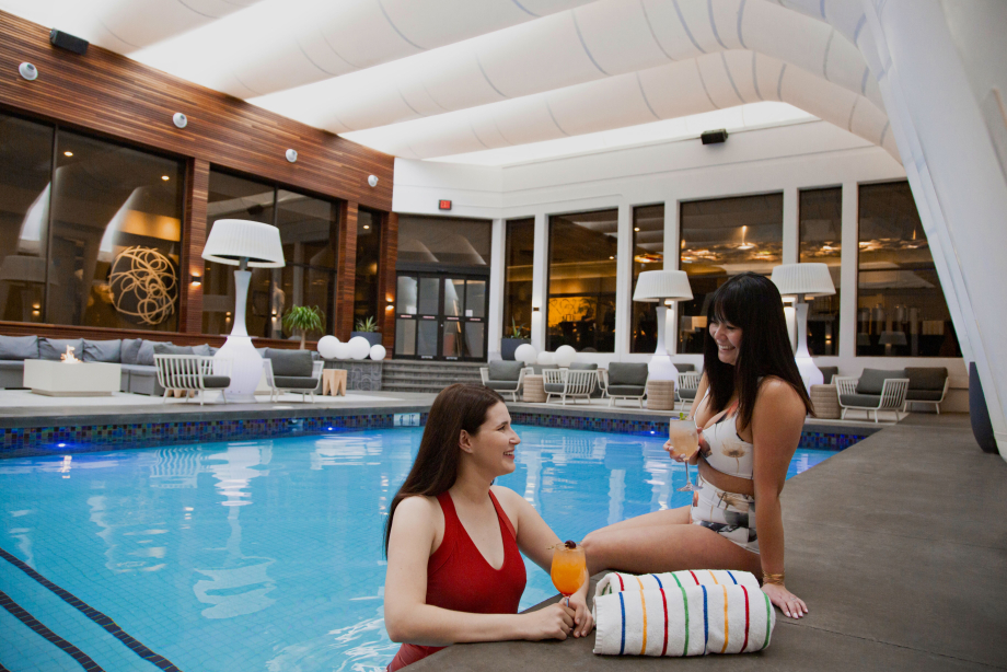 Two women enjoying drinks by the indoor pool at Hotel Arts in Calgary