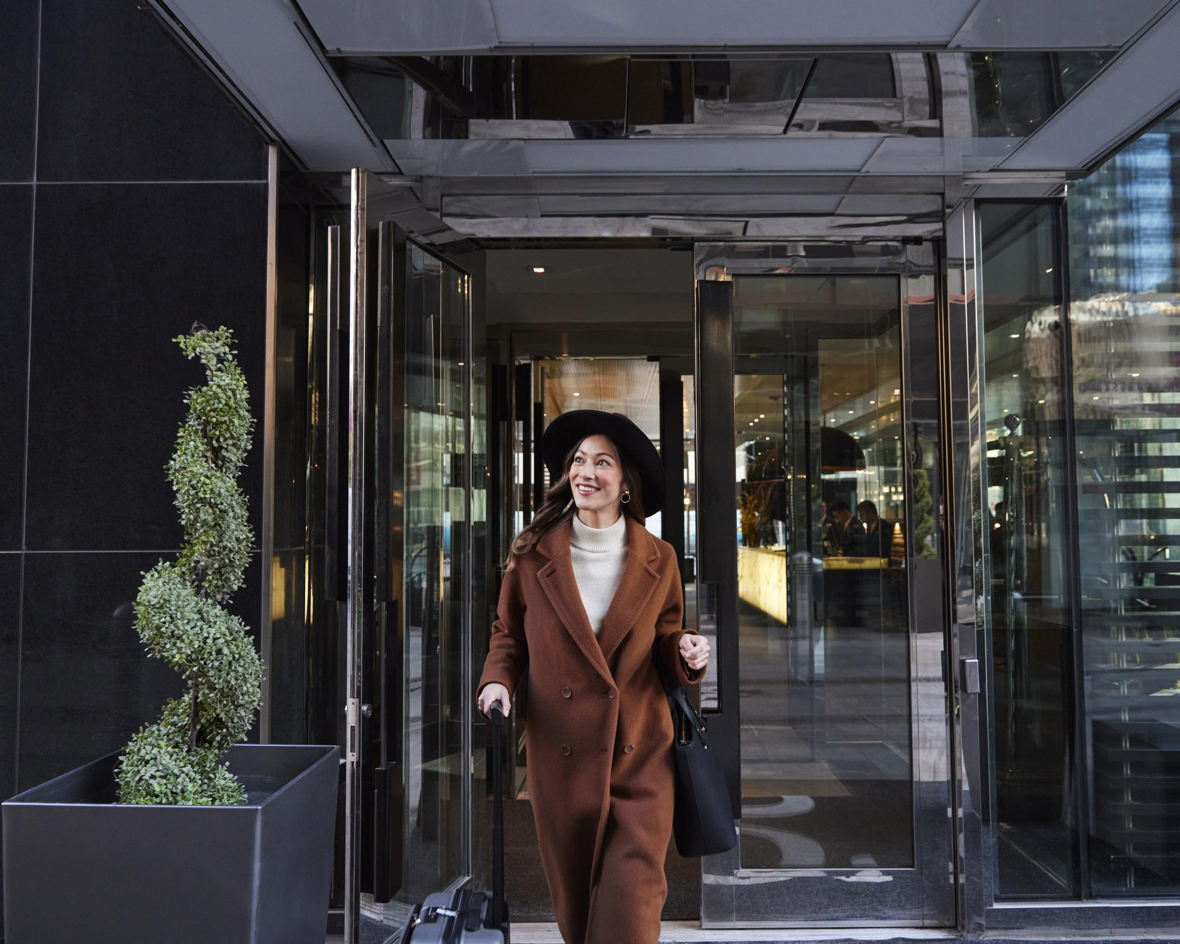 Woman walking with her luggage out of the front doors of Le Germain hotel