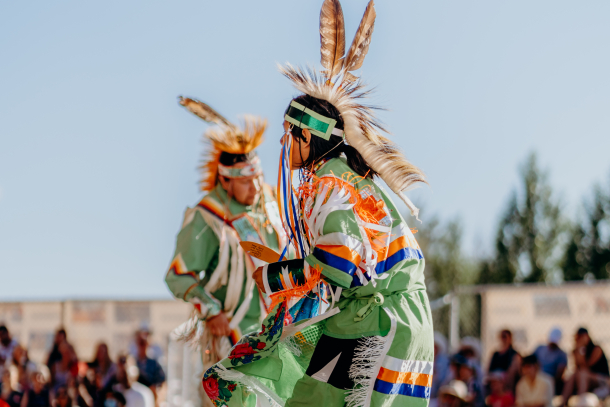 2 indigenous men dressed in traditional attire dancing