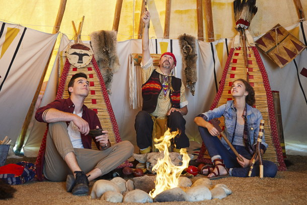 Couple sitting by the fire inside a tipi with an Indigenous man at Heritage Park