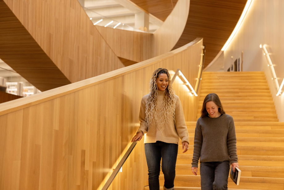 Two women walking down the library staircase with books