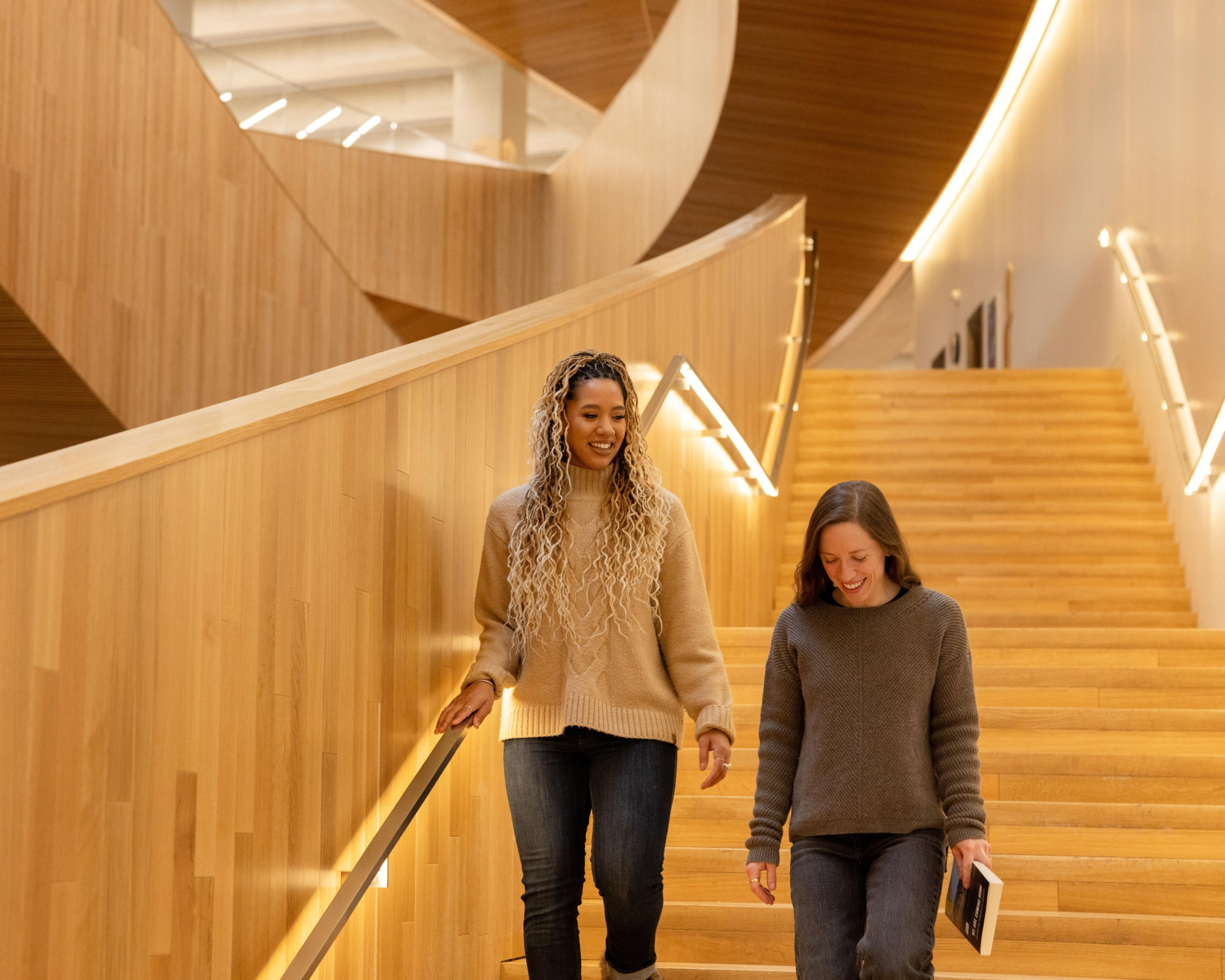Two women walking down the library staircase with books