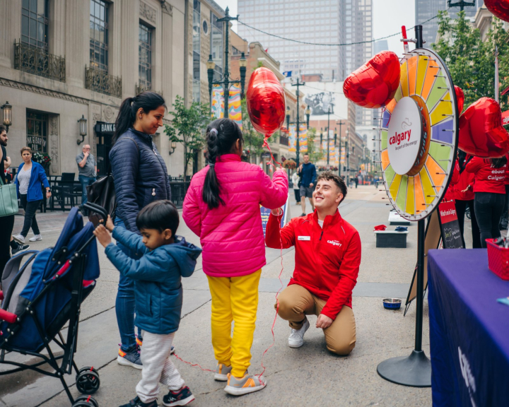 Tourism Calgary staff member handing a balloon to a smiling child on Stephen Avenue.