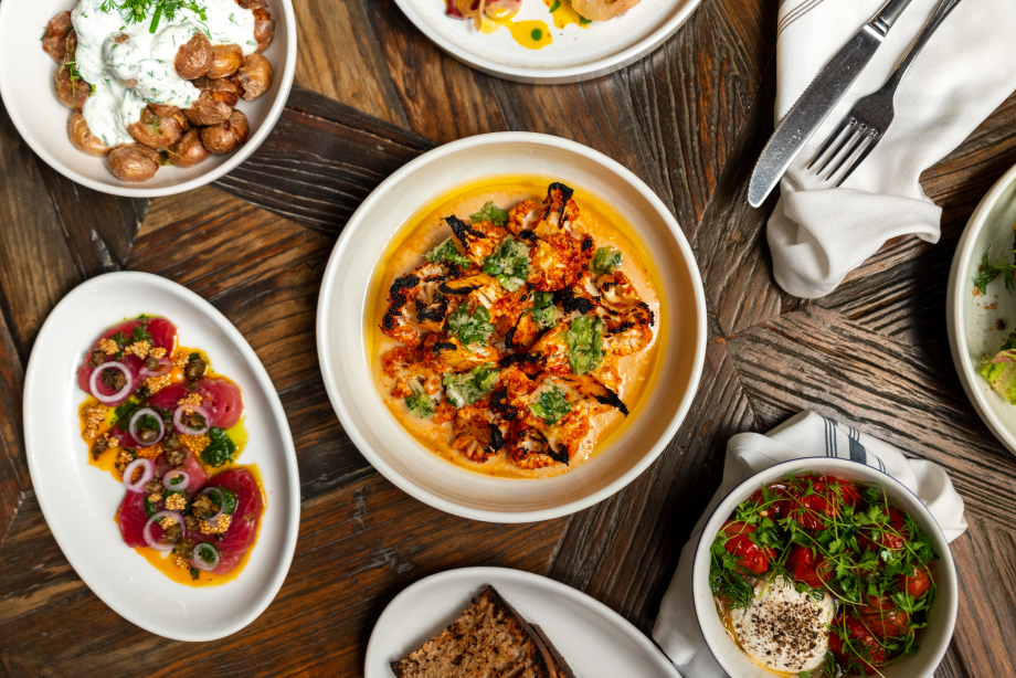 A top down image of a main dish with sides laid out throughout the table with cutlery laid out beside it