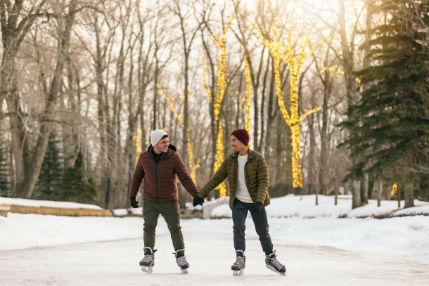 Two men hold hands while ice skating through the lit up trees in Bowness Park in Calgary