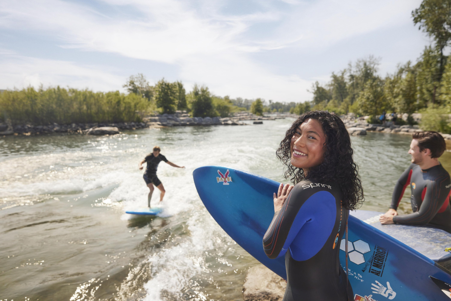 Girl holding her surfboard smiling on the bank of bow river