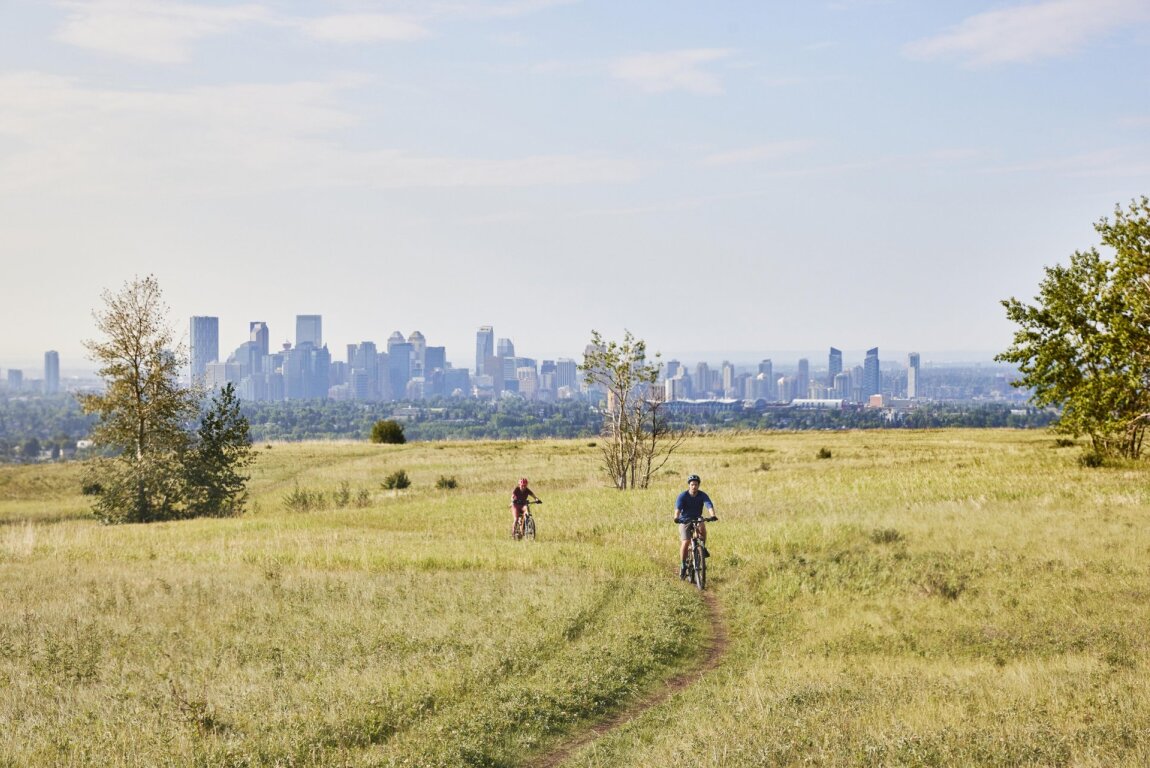 Two people mountain biking at Nose Hill Park with the skyline in the background.