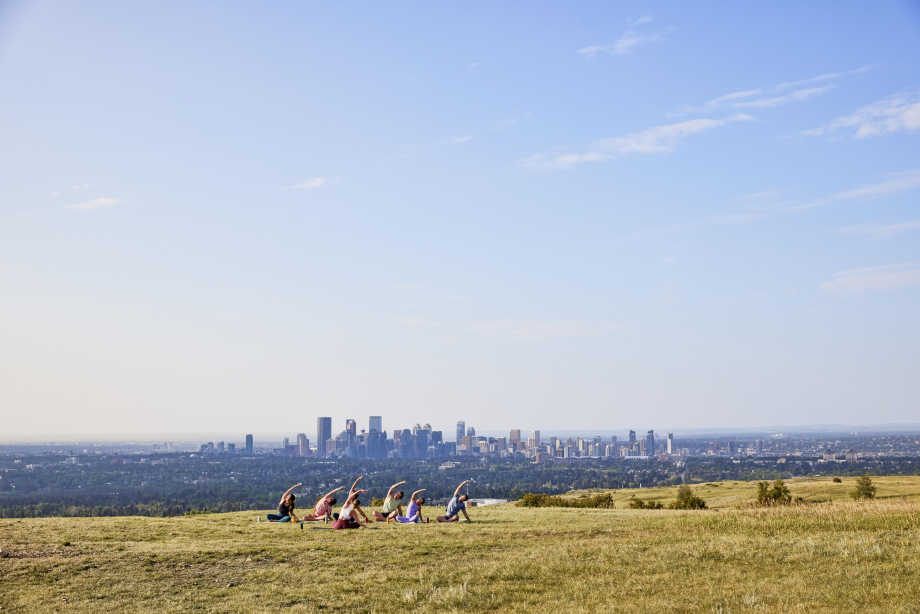 Group of 6 people doing yoga at the top of a hill overlooking the Calgary skyline