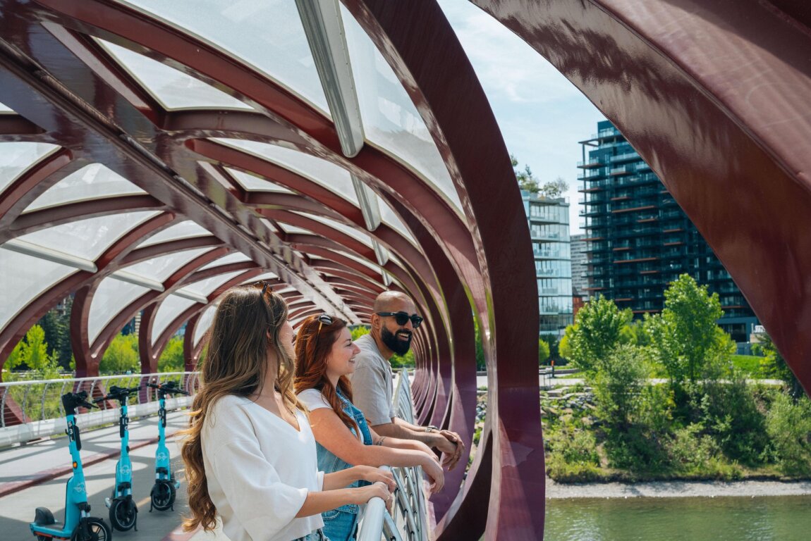 Three friends on the Peace Bridge look out at the Bow River.