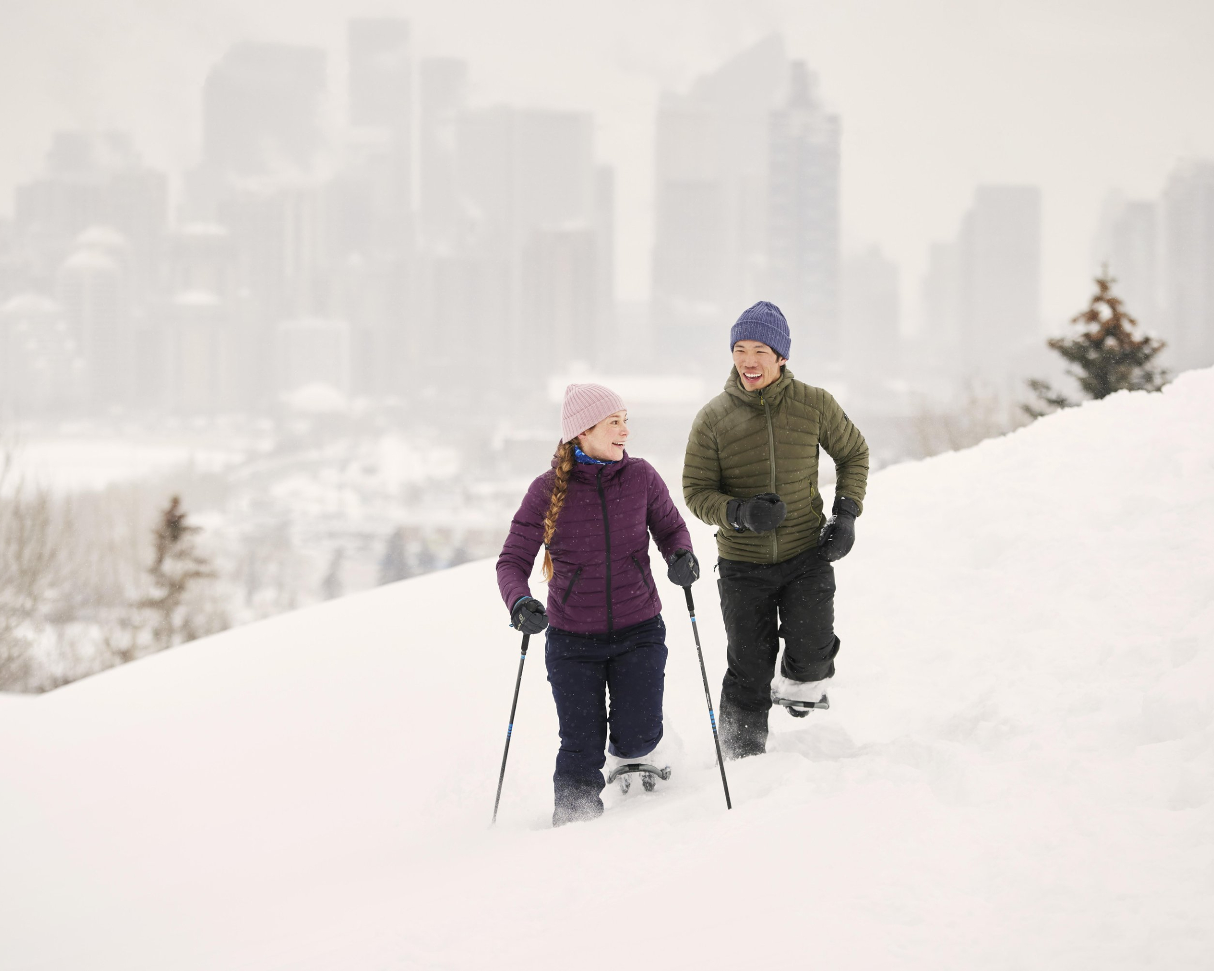 Man and woman snowshoeing in the winter with the Calgary downtown skyline behind them.