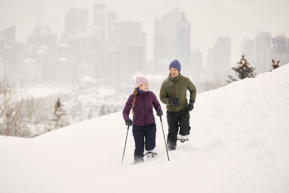 Man and woman snowshoeing in the winter with the Calgary downtown skyline behind them.