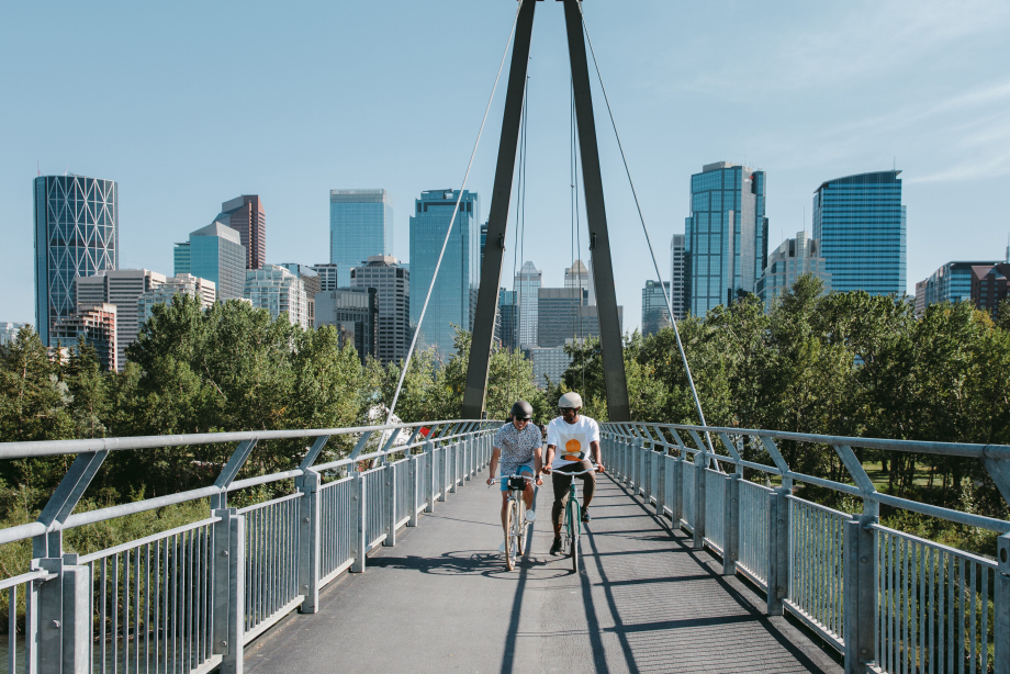 Couple riding bicycles across a bridge with downtown Calgary in the background
