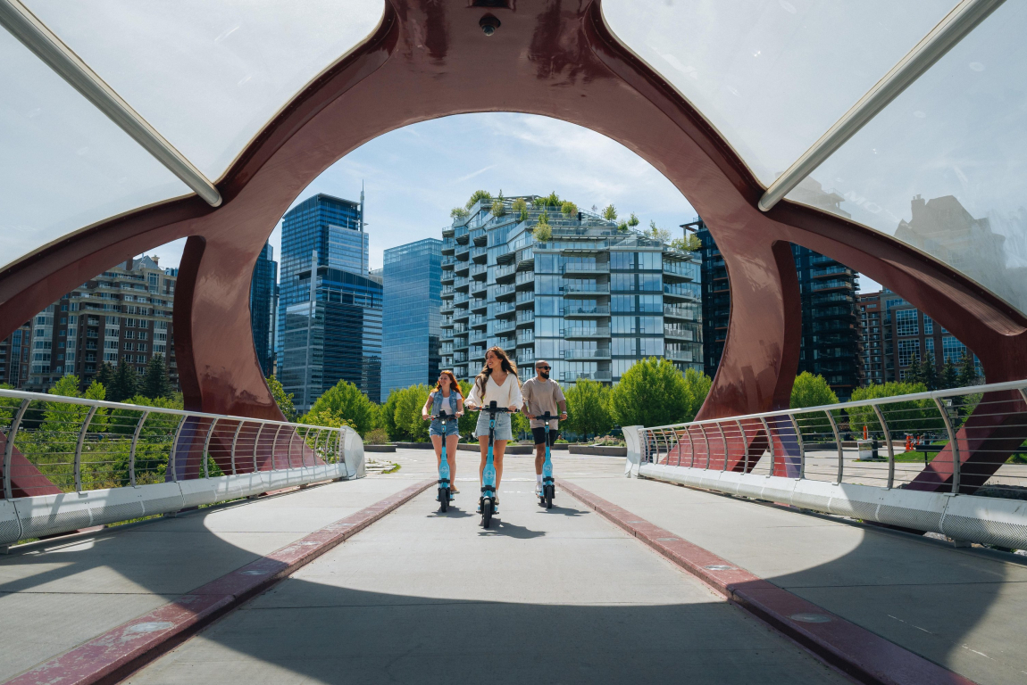 3 friends on e-scooters on the peace bridge in Calgary