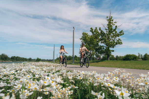 A male and a female cycling on a summer day along the bow river pathway in East Village