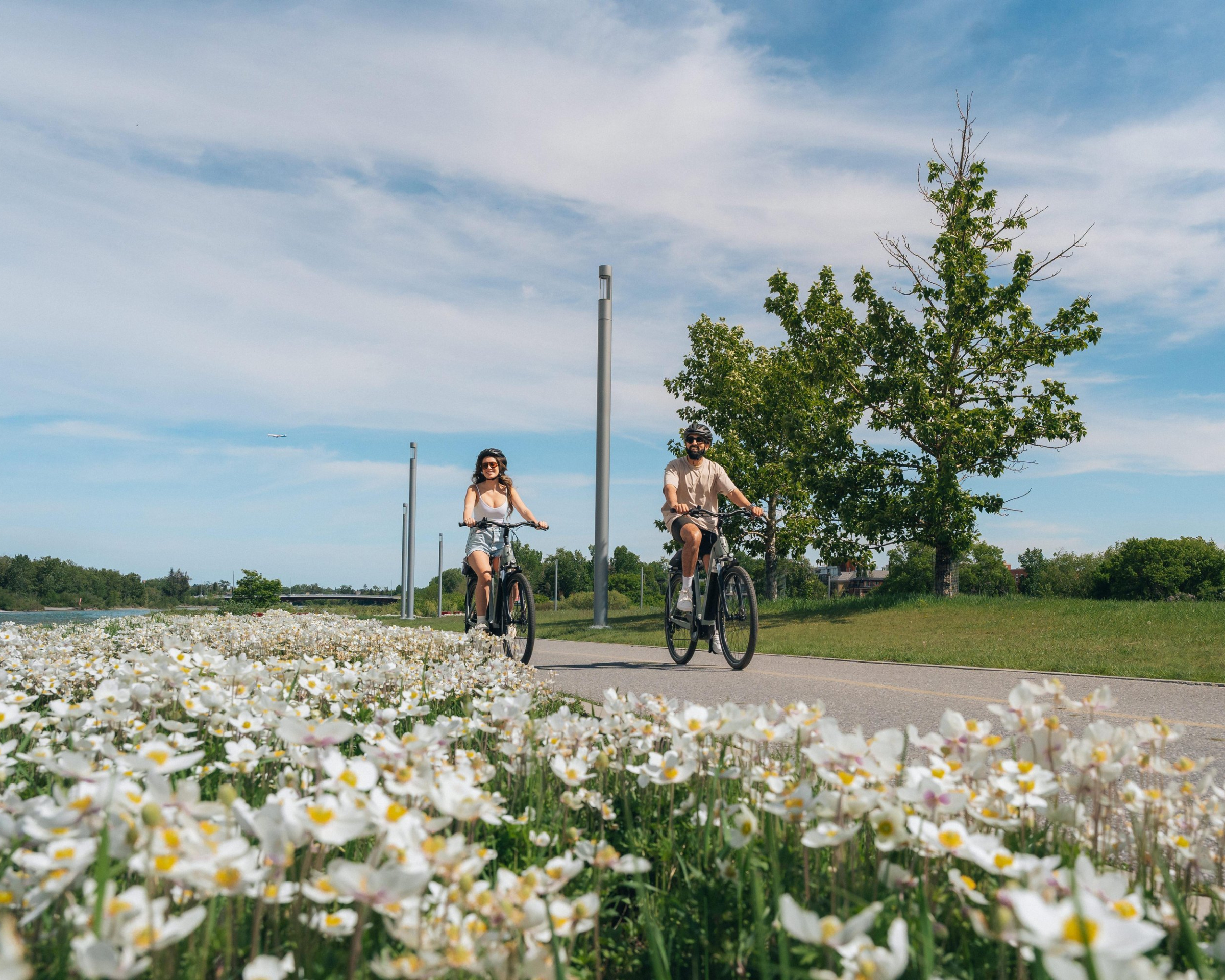 A male and a female cycling on a summer day along the bow river pathway in East Village