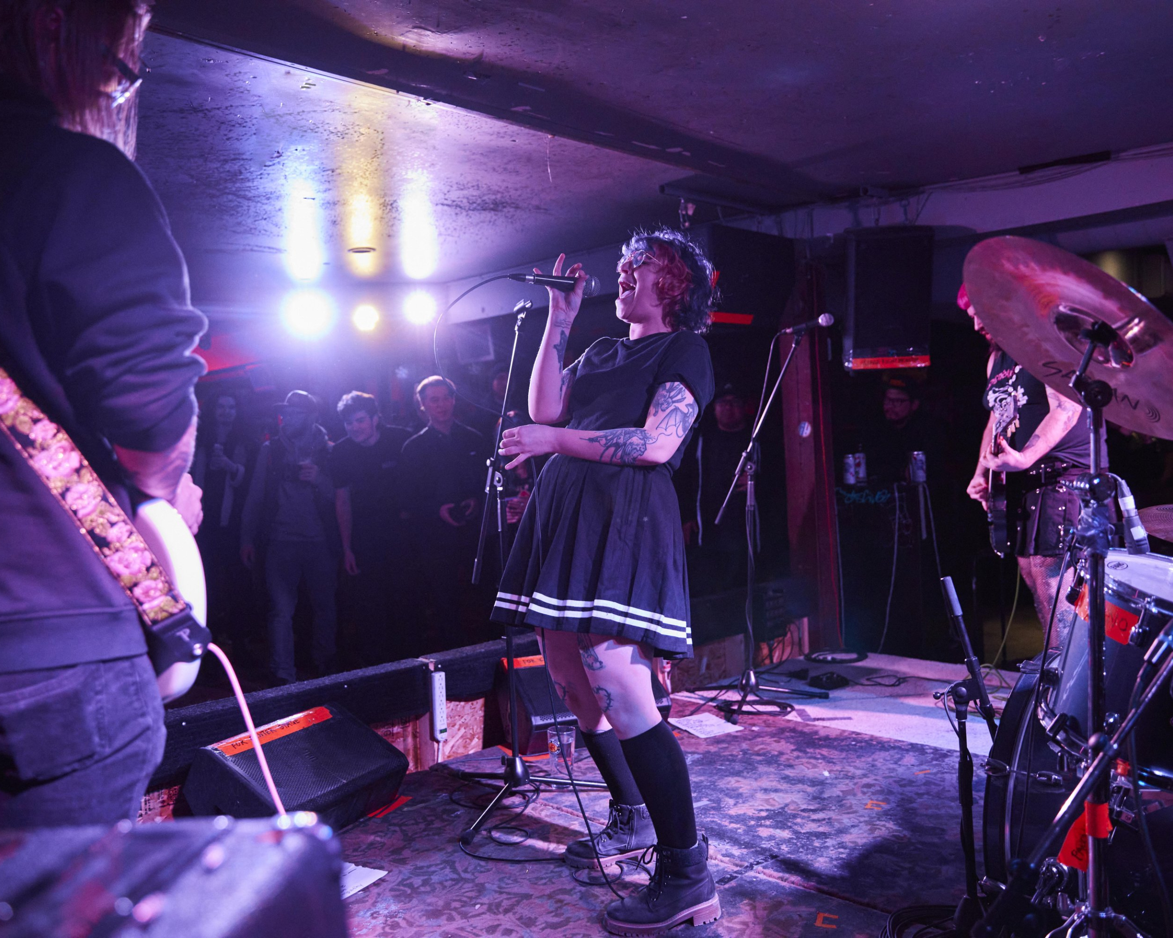 Woman singing into mic on stage with guitarists and fans in the background